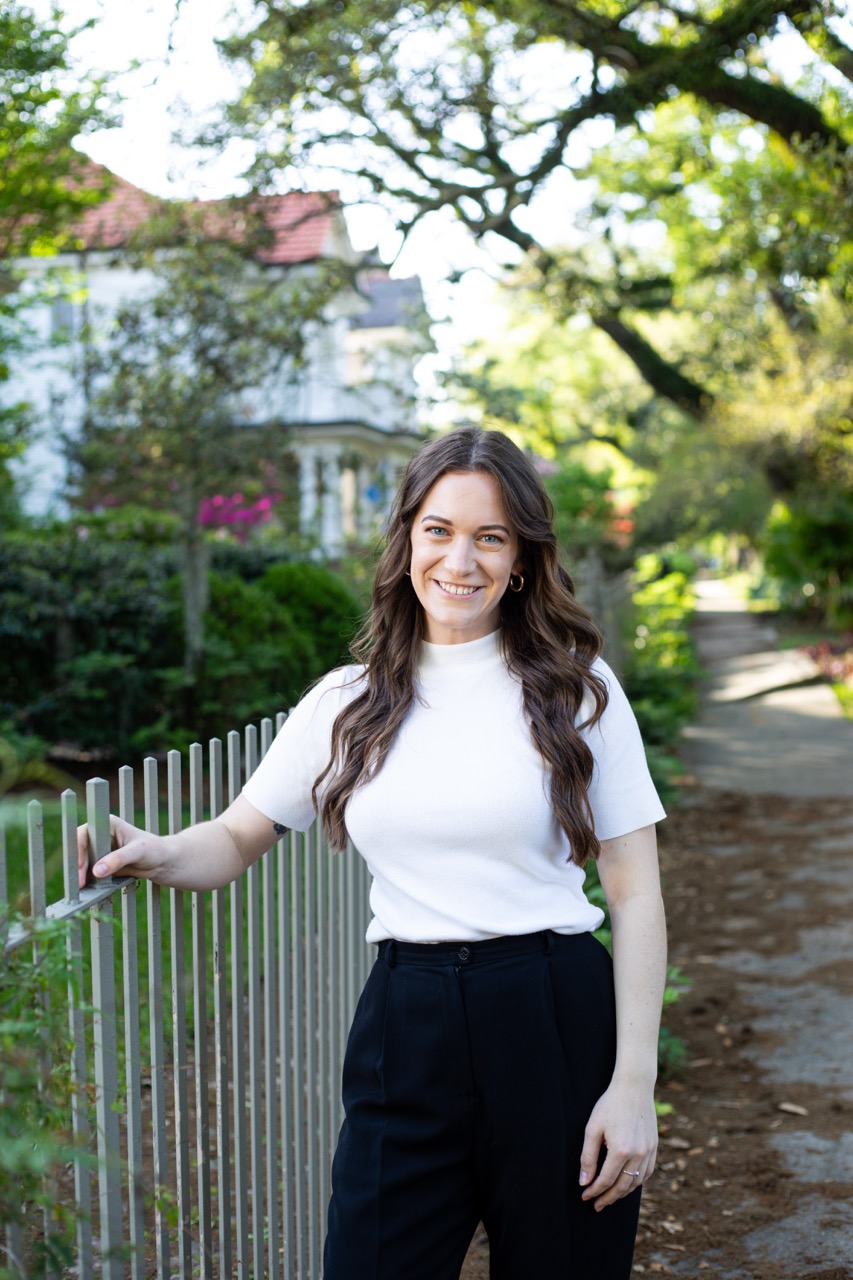 Jesse Coleman, REALTOR® with Keller Williams Realty New Orleans, standing by a white picket fence in front of a historic New Orleans home