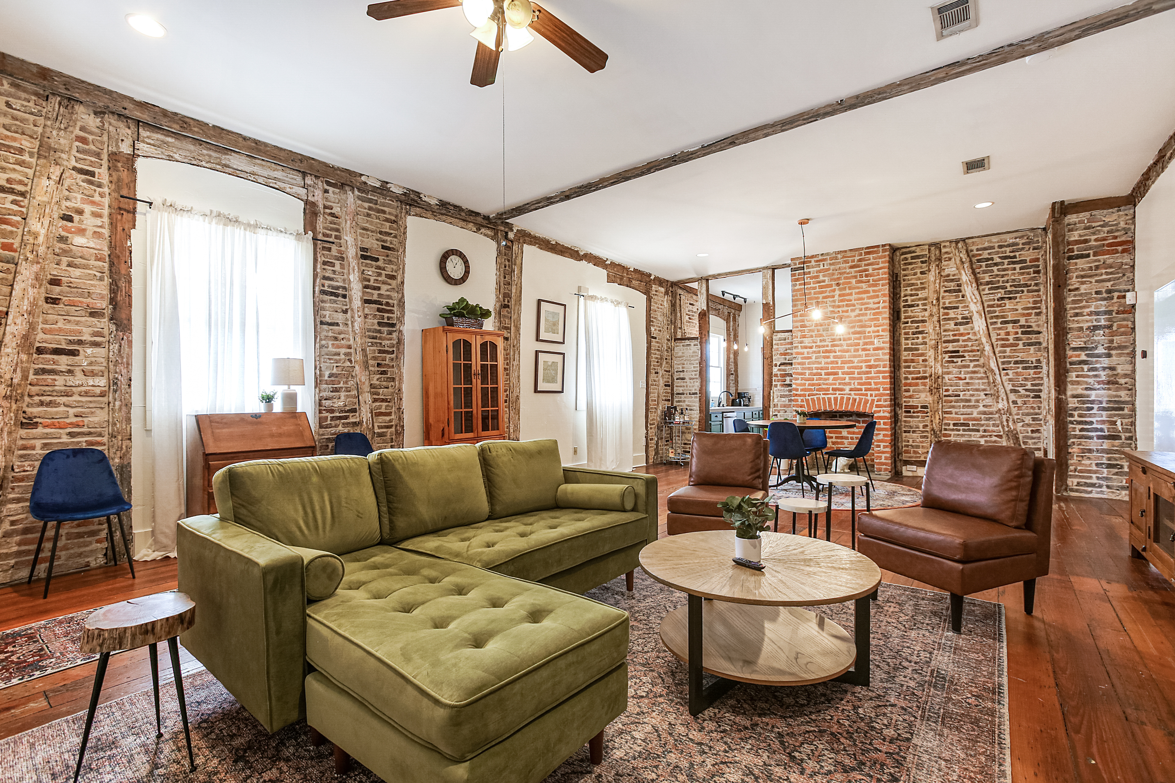 Furnished living room with a green velvet sectional and exposed brick walls in a New Orleans mid-term rental