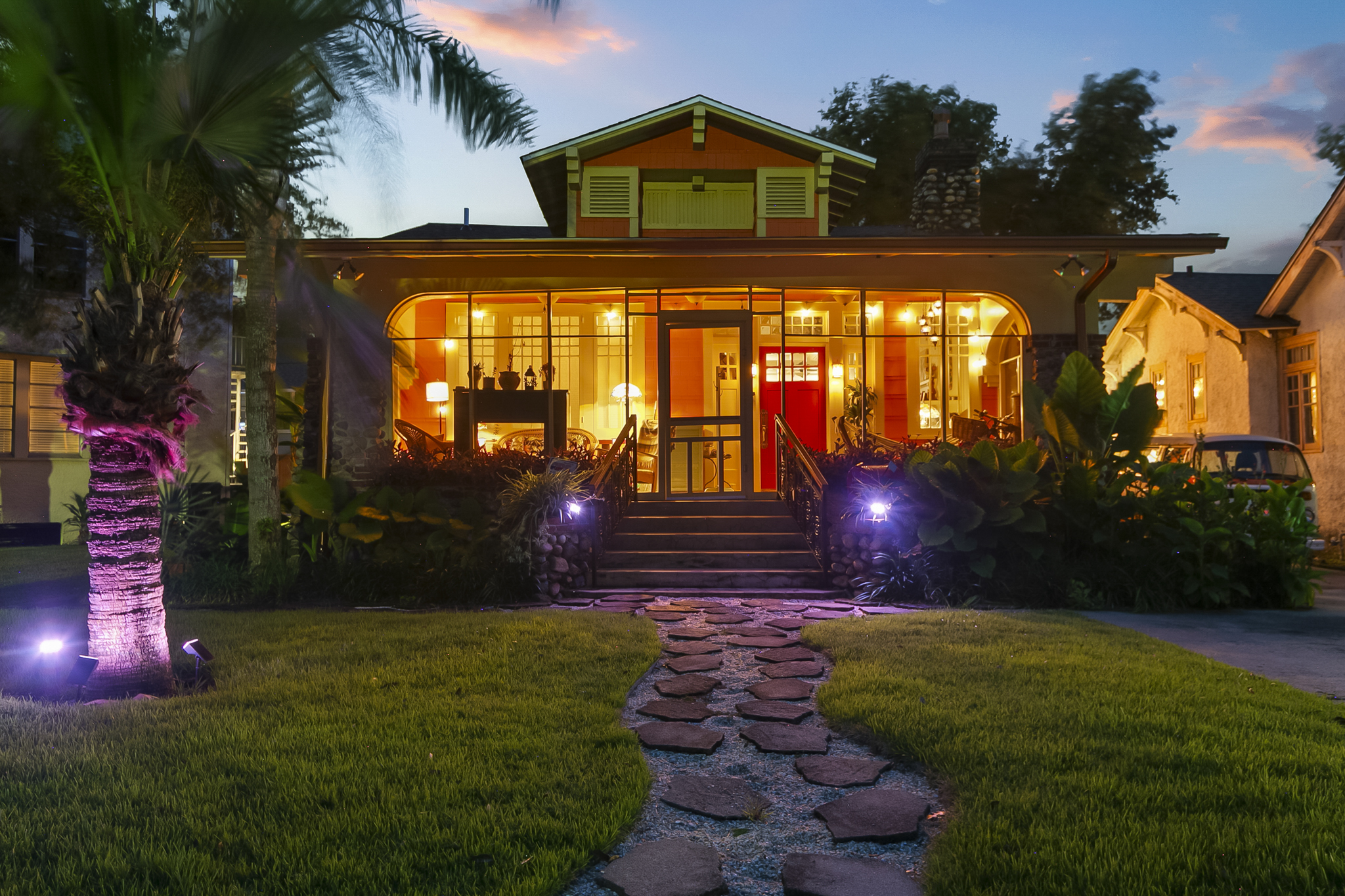 A New Orleans bungalow glowing warmly at twilight, lit windows and a stone path through the front garden