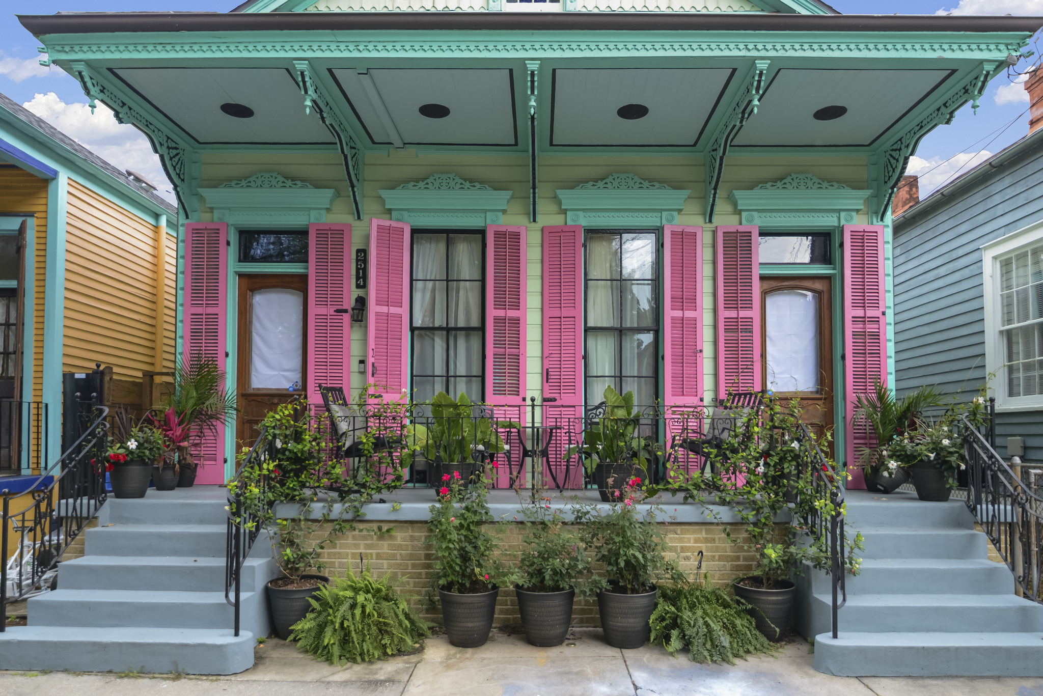 Colorful historic New Orleans shotgun home with pink shutters and a teal porch on a walkable neighborhood street